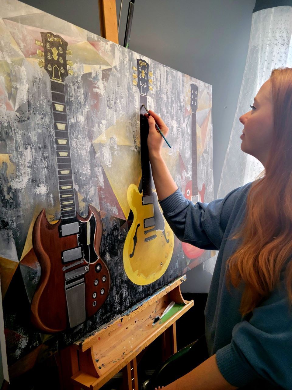 Image of Brittany Cosgrove painting three guitars.  The painting is on a wooden easel.