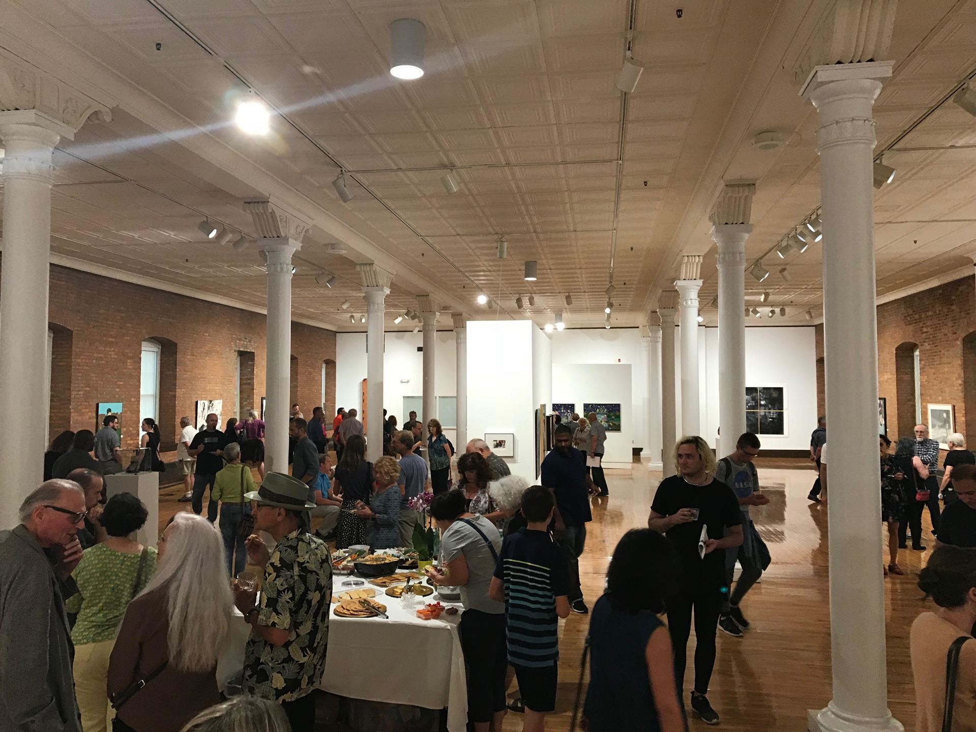 Art opening at Fort Hayes Shot Tower Gallery. A group of people are talking in little groups while others look at art and fill their plates with food.